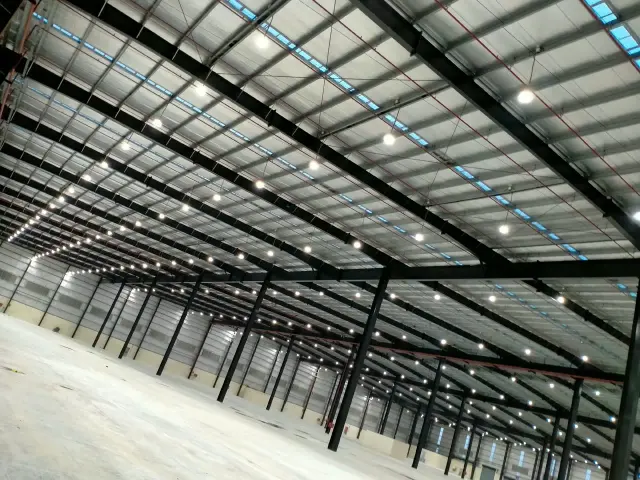 Wide view of a PEB warehouse interior with roof trusses and pendant lighting